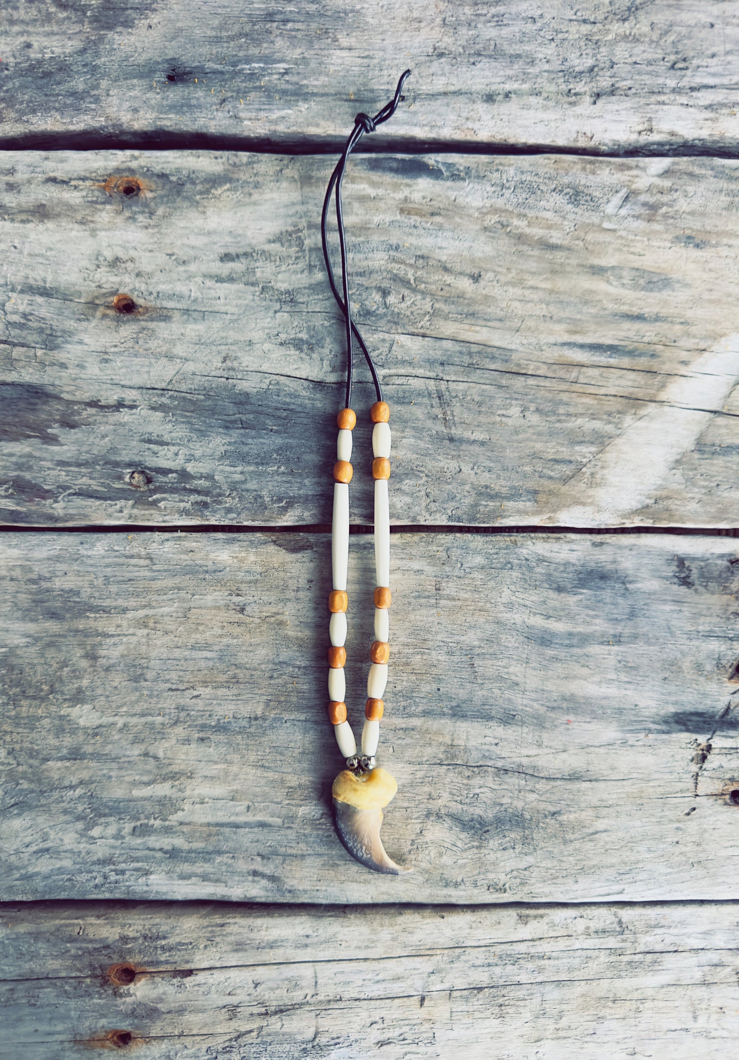 Close-up of bear claw necklace with bone and wooden beads displayed on rustic wood background